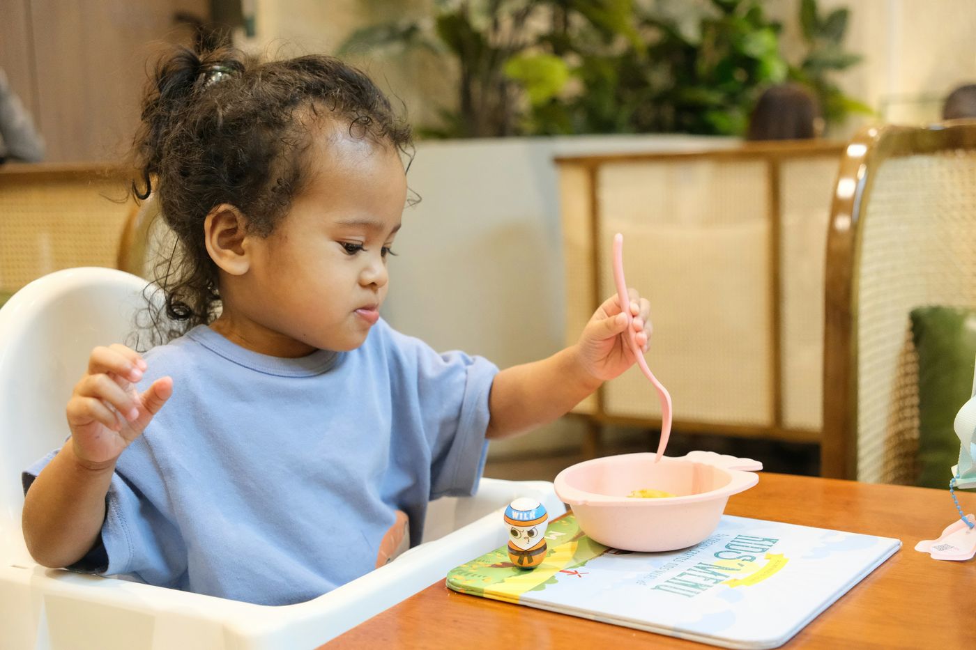 A young child self-feeding with a fork in a high chair